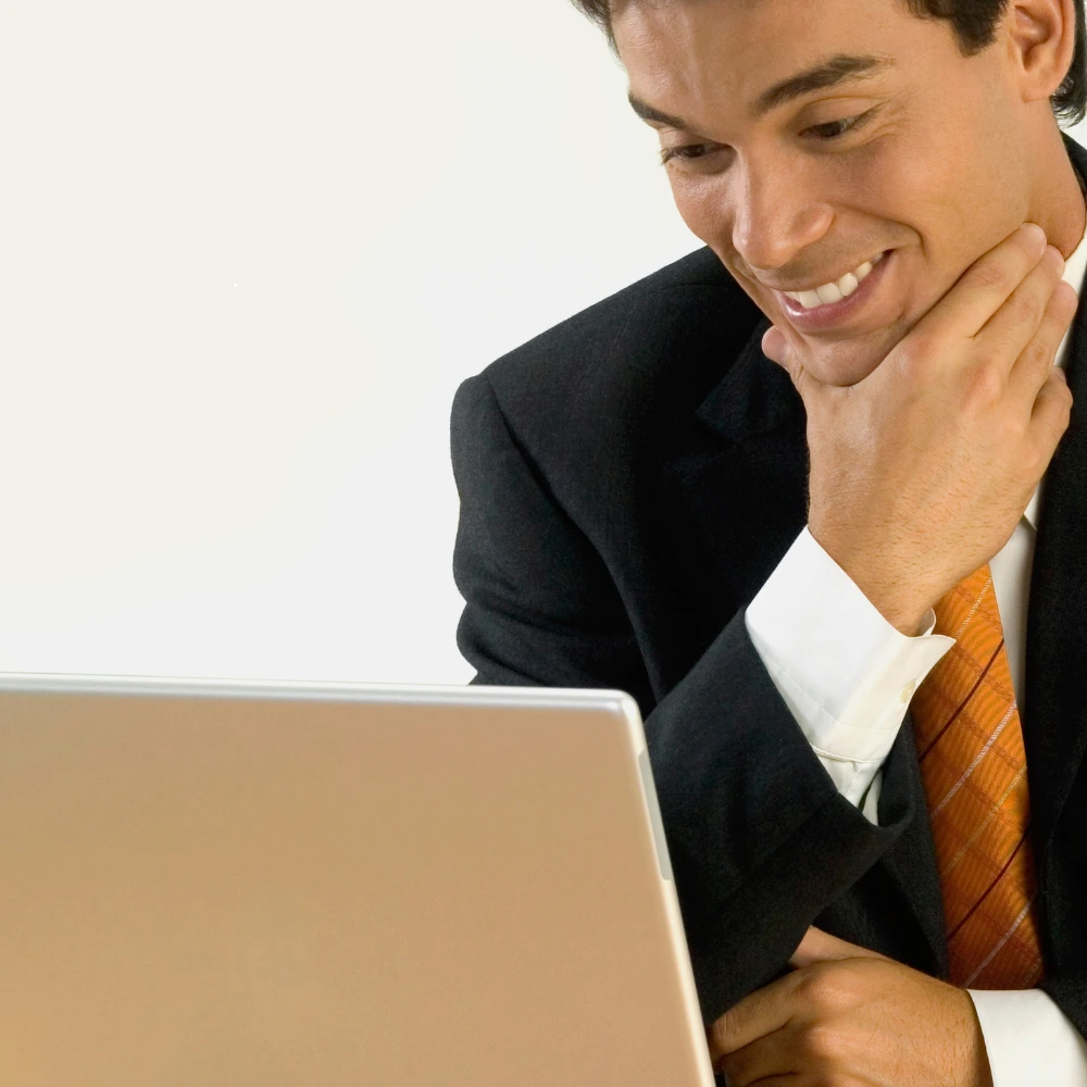 A smiling businessman in a suit and orange tie looking down at a laptop screen.