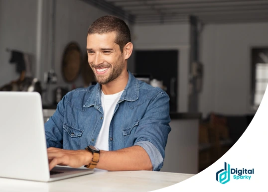 A smiling man with a beard working on a laptop, appearing happy and engaged, with the Digital Sparky logo in the corner.