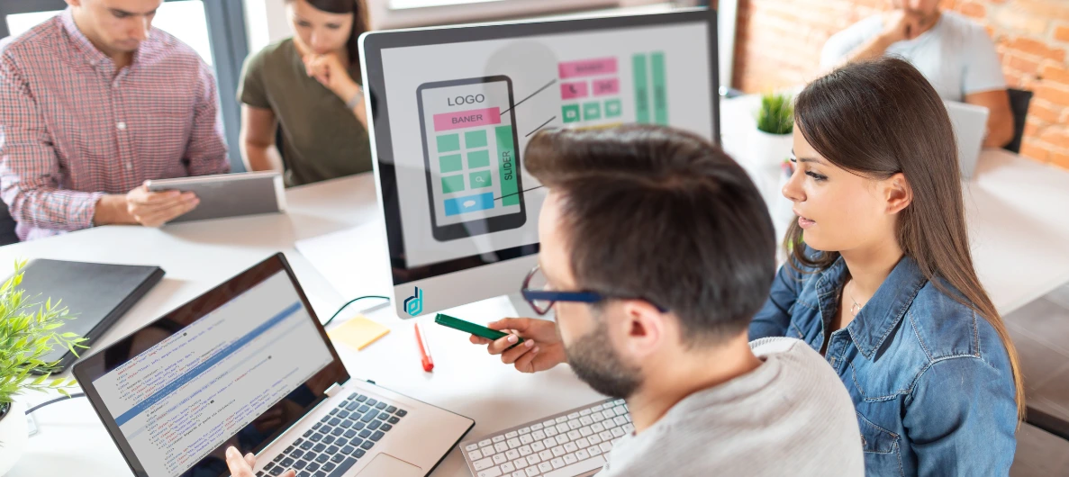 Team members in an office setting discussing UI/UX design and front-end development, with a focus on screen displays.