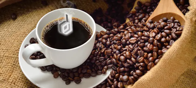 A white coffee cup with steam rising and the Digital Sparky logo in the foam, sitting on a saucer amidst scattered coffee beans and a burlap sack with a wooden scoop of beans.