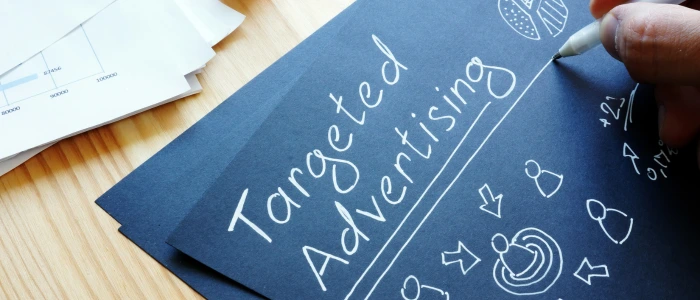 A hand writing "Targeted Advertising" on a dark blue paper with various marketing-related doodles.